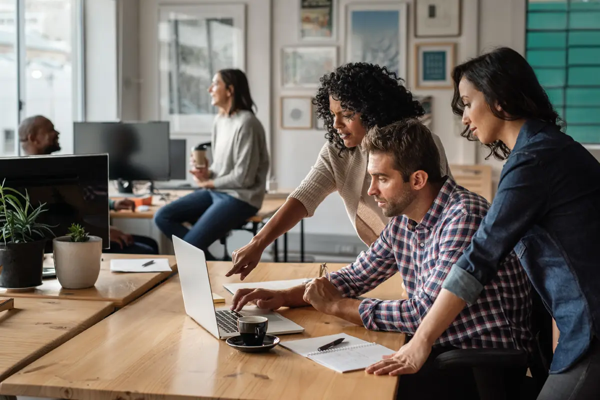 Three co-workers talk as they work at a laptop together
