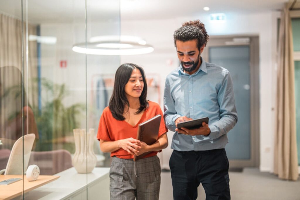 A man shows a woman something on his hand-held device in an office setting